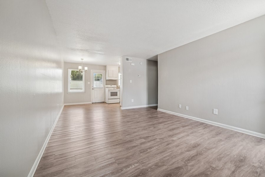 A spacious room with wood flooring and a kitchen in the background.