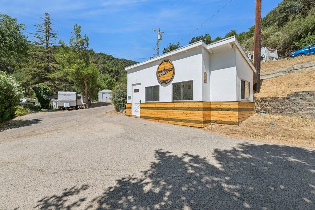 A small white building with a yellow sign on the front is situated on a gravel road.