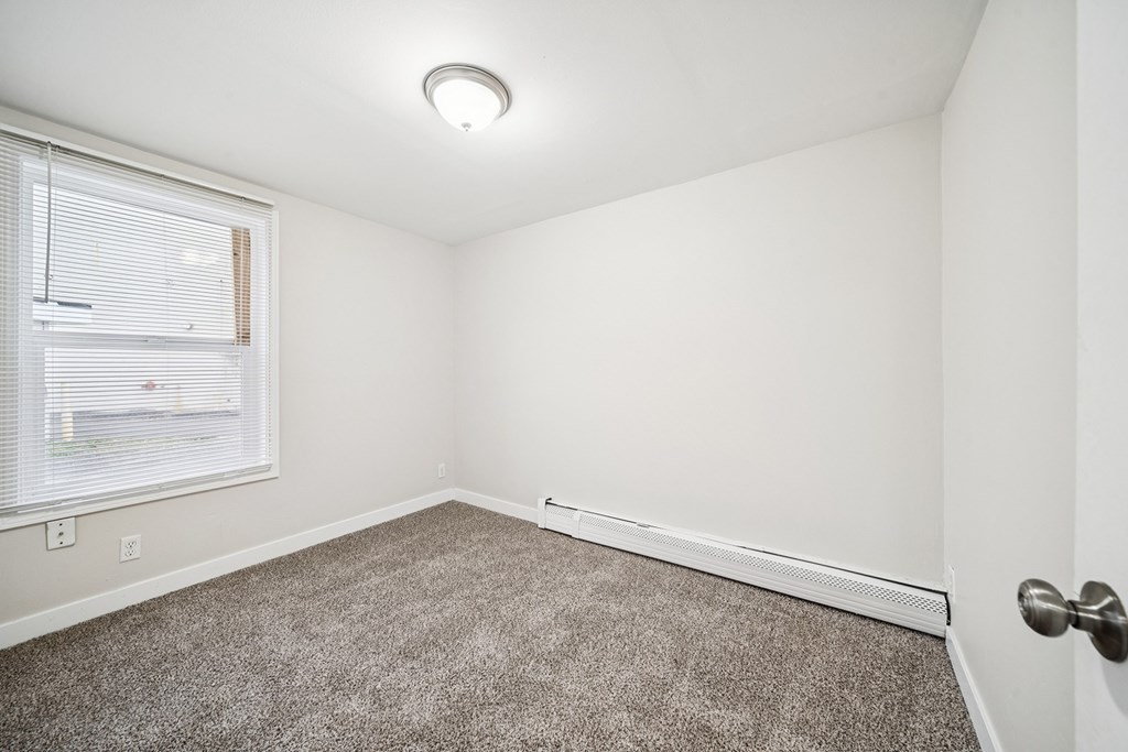 A room with a carpeted floor and a window with blinds.