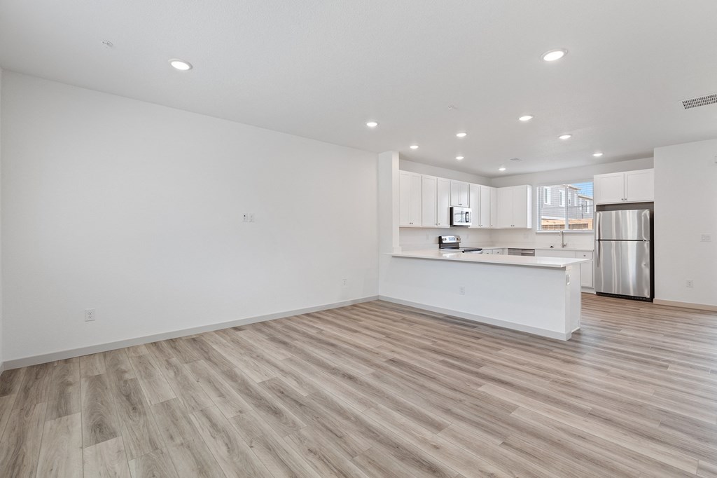an empty living room and kitchen with white walls and wood flooring