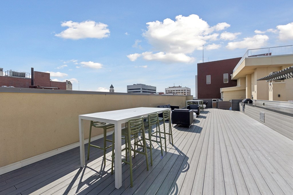 A table and chairs are on a wooden deck with buildings in the background.