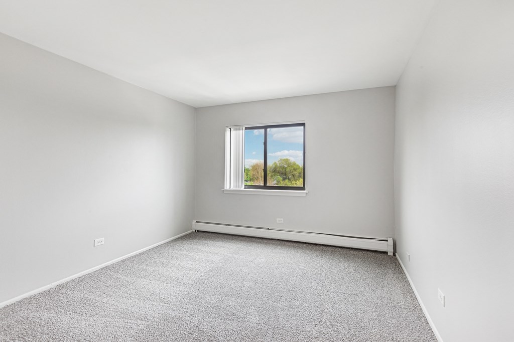 A bedroom with a window and a carpeted floor.