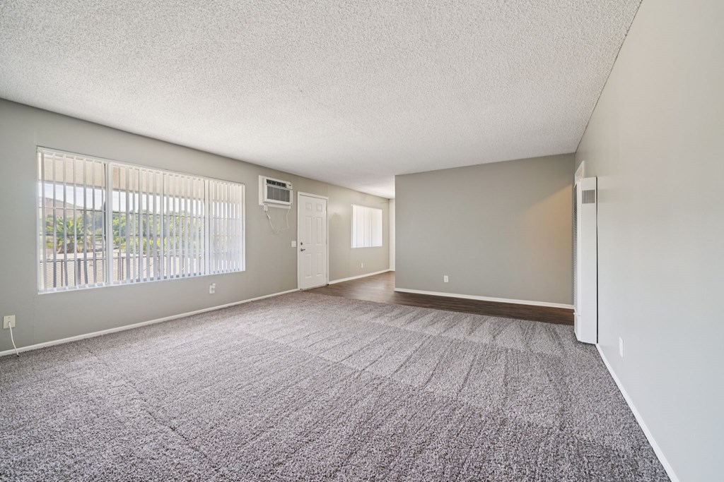 A spacious room with a carpeted floor and a window with blinds.