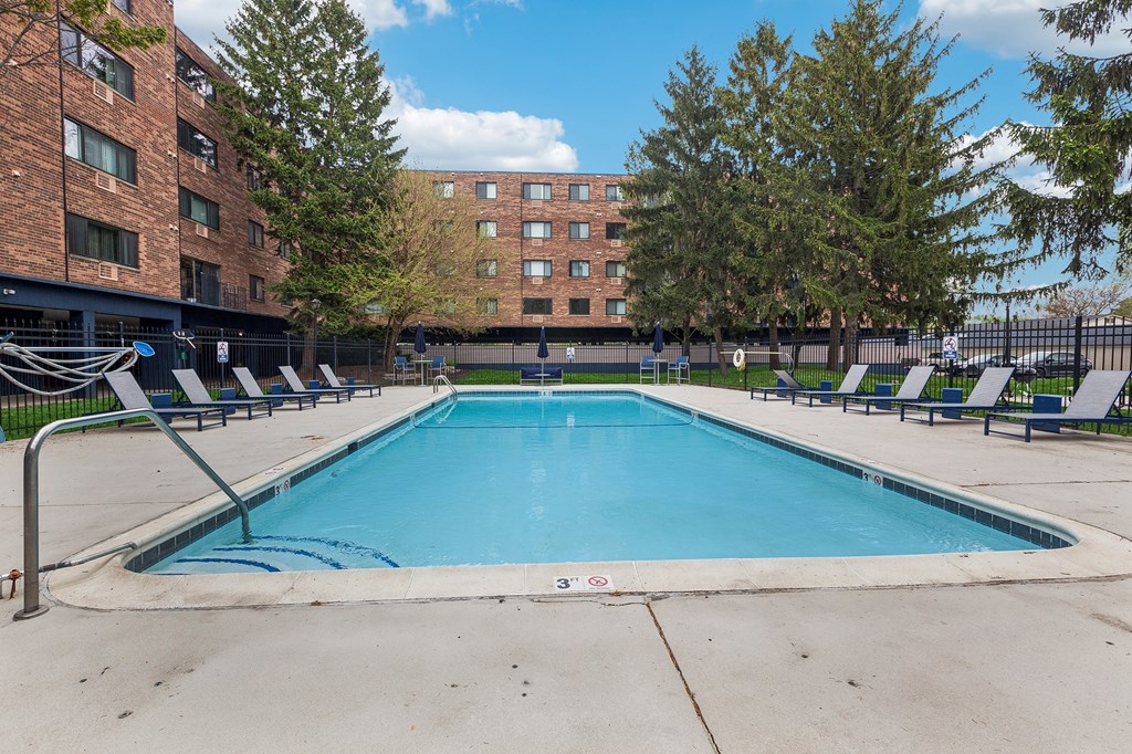 A swimming pool in front of a brick building with trees around.
