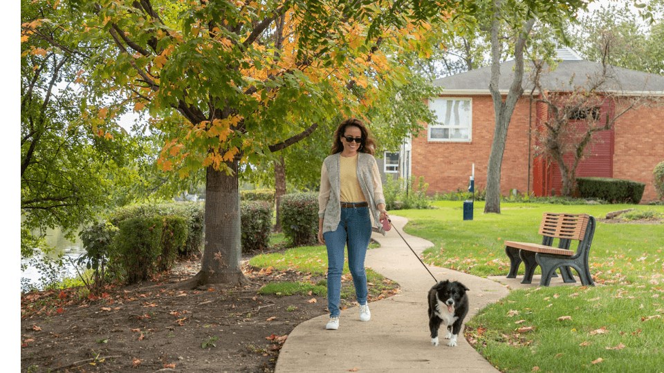 a woman walking a dog on a leash on a sidewalk  at The View Apartments St Charles, St Charles, Illinois