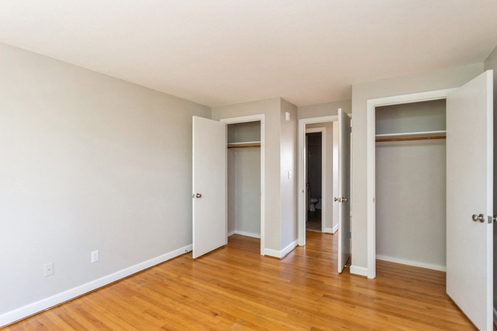 an empty bedroom with wood floors and closet doors