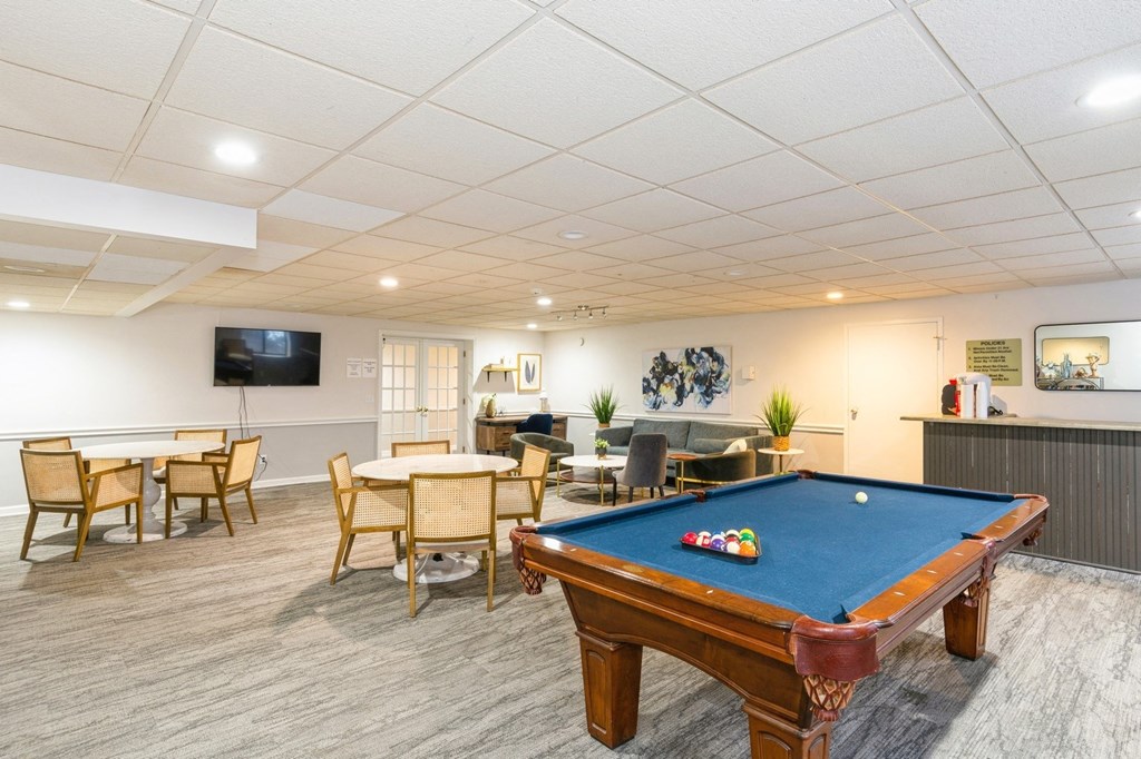 A pool table is in the middle of a room with a TV and a dining table.