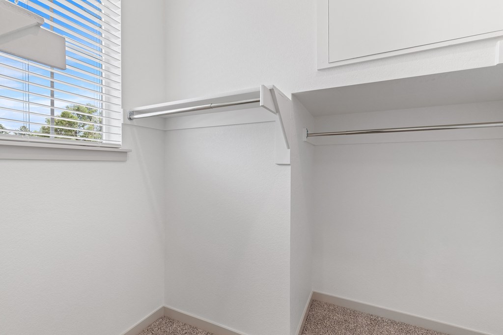 a walk in closet in a white room with a window