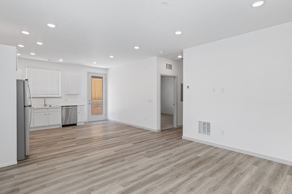 an empty living room and kitchen with white walls and wood flooring