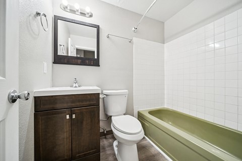 A white toilet sits next to a green bathtub in a bathroom.