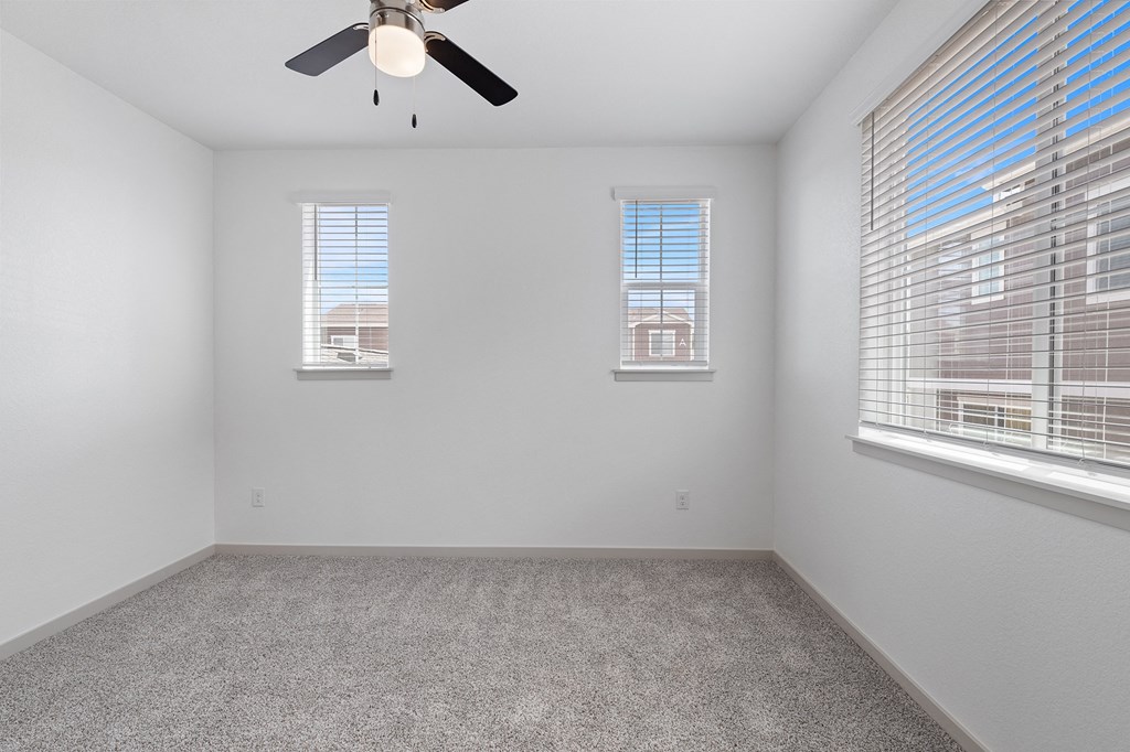 an empty room with two windows and a ceiling fan