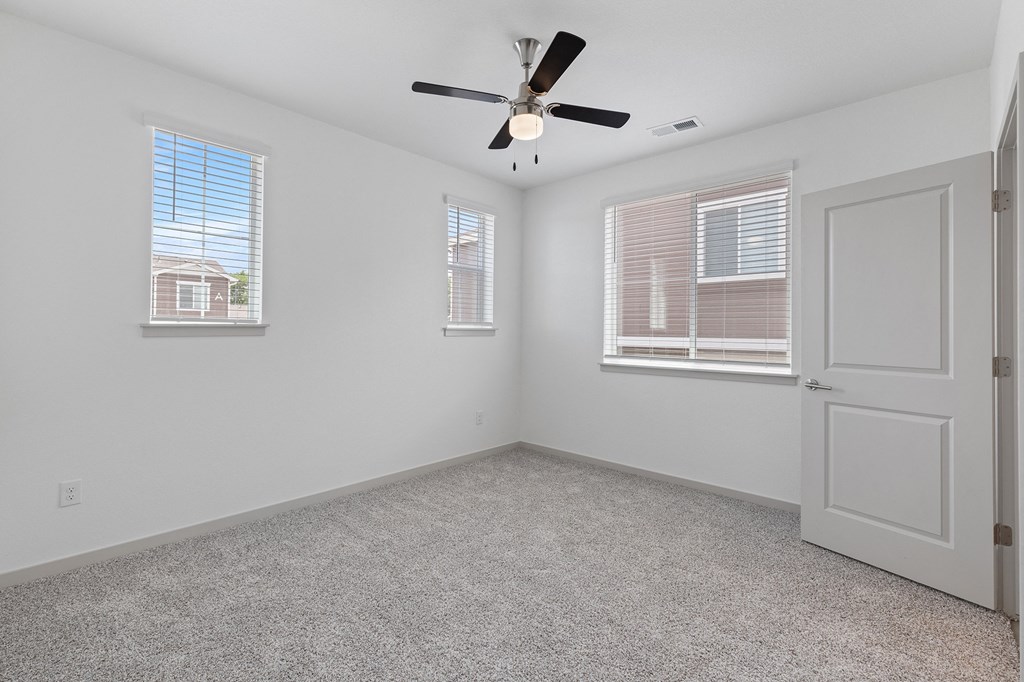 an empty room with a ceiling fan and two windows