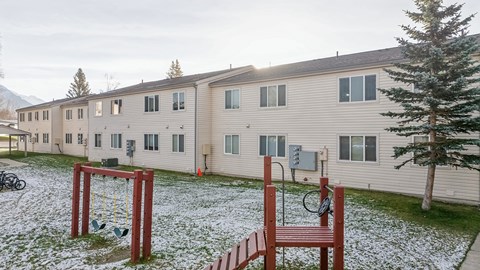 A playground with a swing set and a basketball hoop in front of apartment buildings.