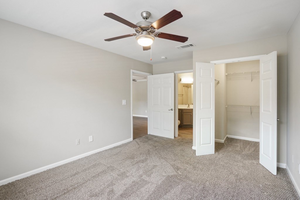 A bedroom with a ceiling fan and carpeted floor.