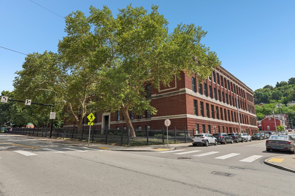 A street view with a red brick building, cars, and trees.