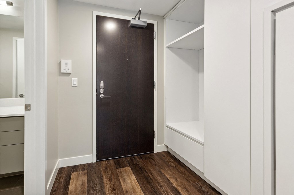 a wardrobe with a wooden door in a room with white walls and wood flooring at The Rowe, Grand Rapids, 49503