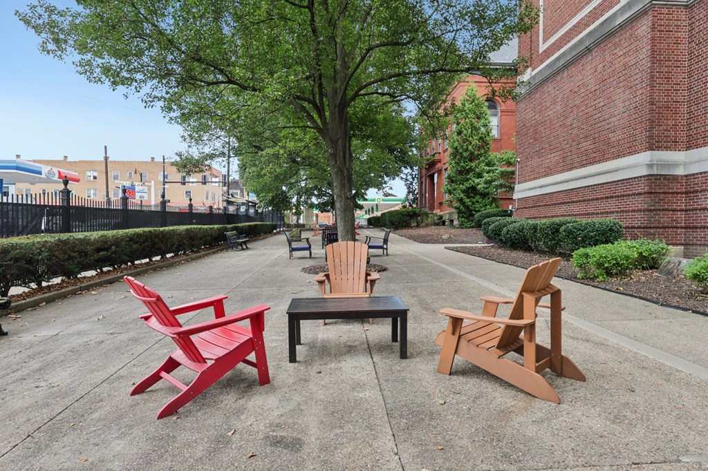 Two brown and one red chair sits on a concrete surface next to a tree and two other chairs.