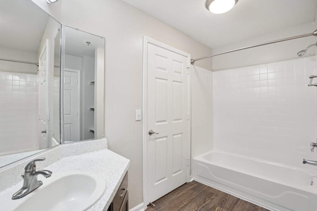 A white bathroom with a sink, mirror, and bathtub.