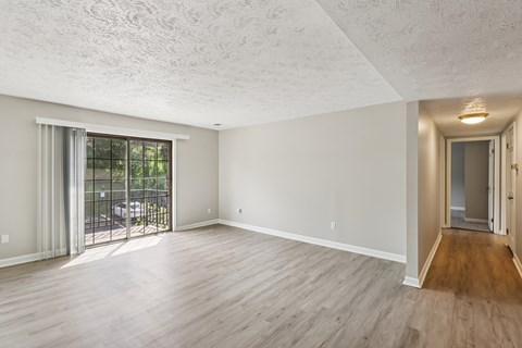 A spacious room with wooden flooring and a sliding glass door leading to a patio.