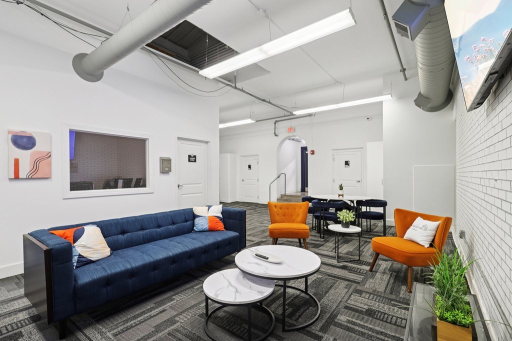 A blue couch is in the middle of a room with orange chairs and a white table.