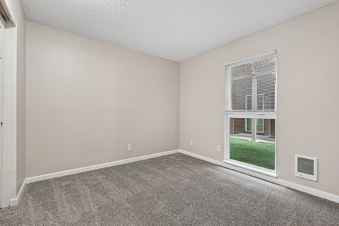 A room with a carpeted floor and a window showing a view of a building outside.