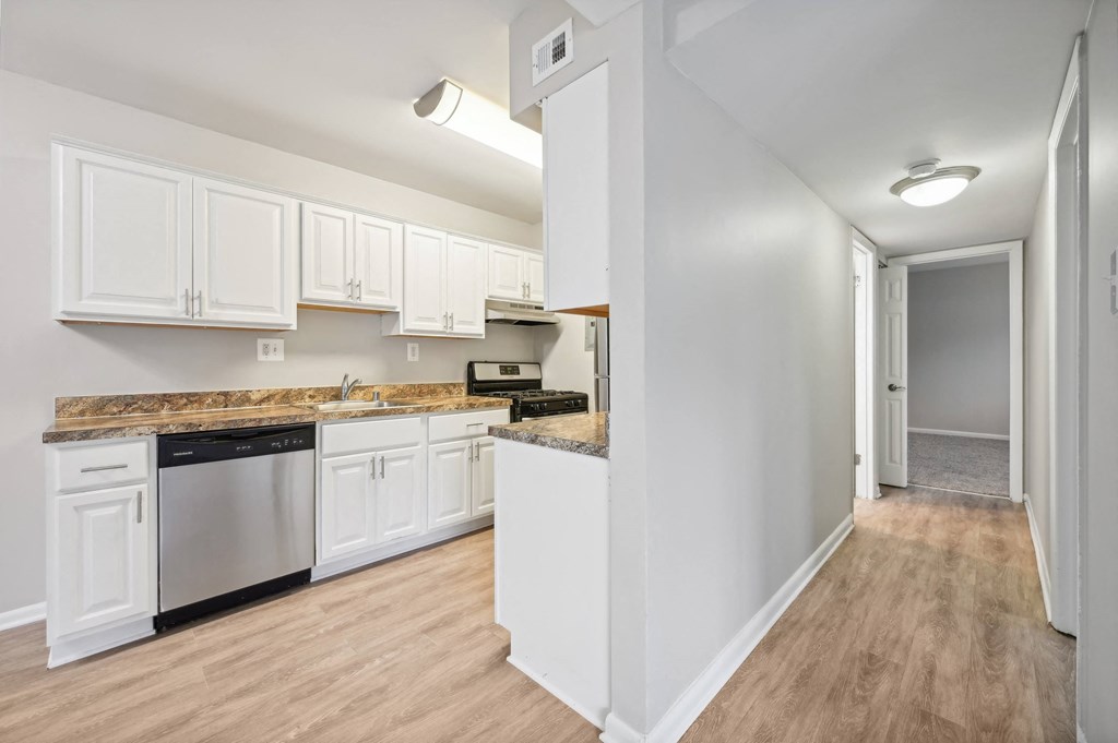 a kitchen with white cabinets and a counter top and looking into a hallway at ReNew Odenton