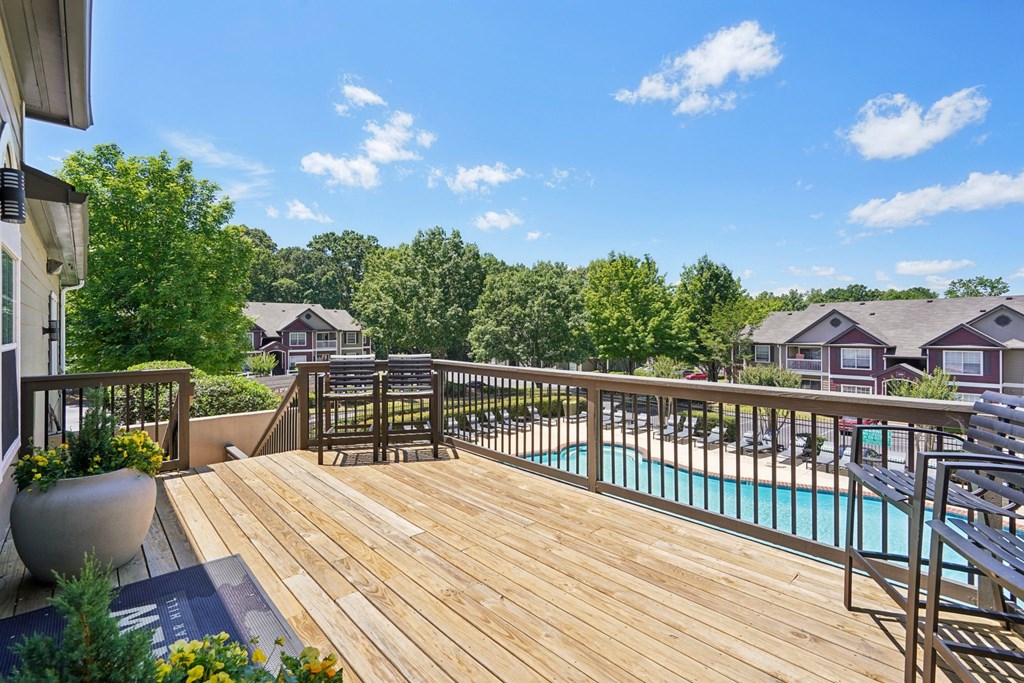 A wooden deck overlooking a pool and chairs.