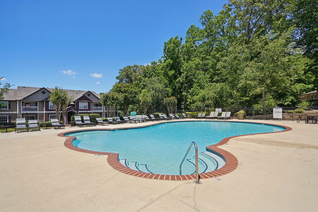 A large swimming pool surrounded by trees and chairs.