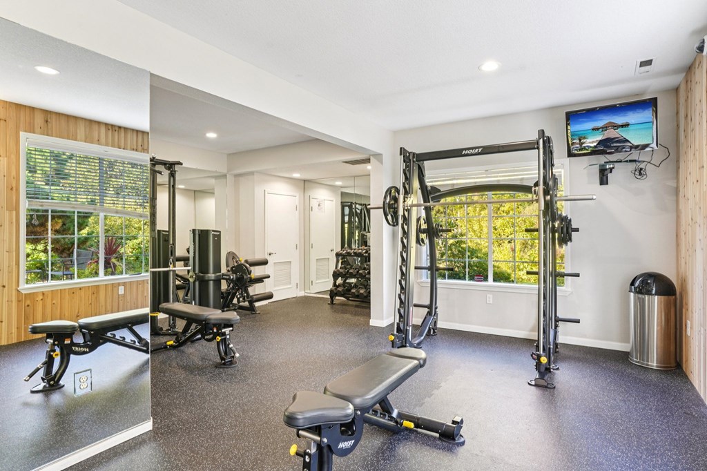 Fitness center with a variety of equipment including a bench, weights, and a television.
