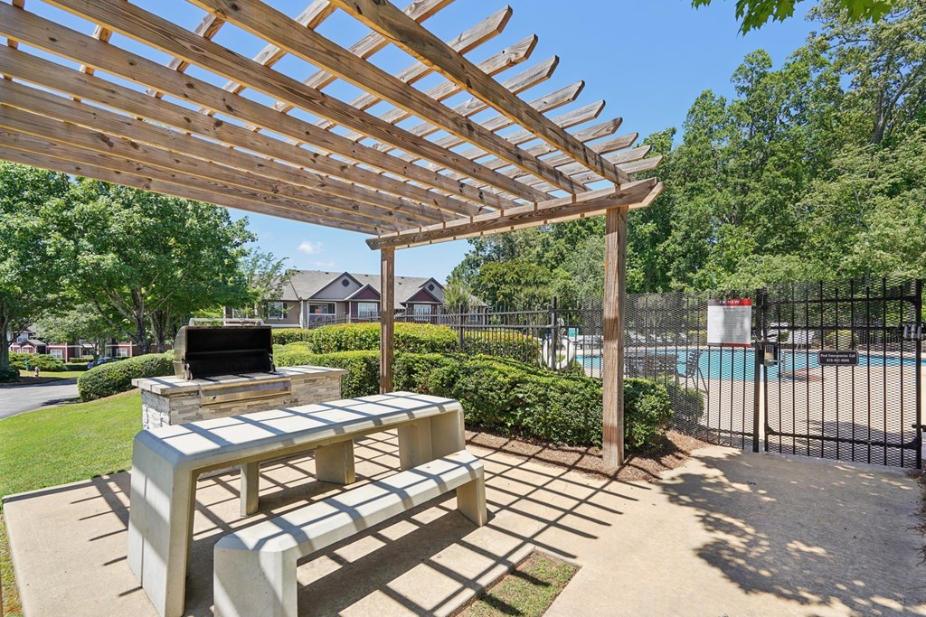 A grilling area with a wooden pergola over a concrete bench in a backyard.