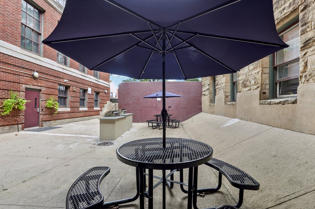 A purple umbrella is open over a table with two chairs.