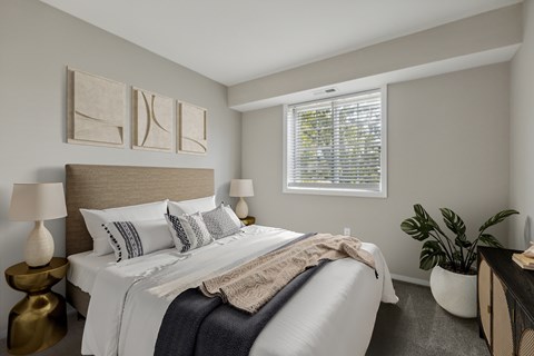 A bedroom with a bed, two lamps, a window, and a plant.