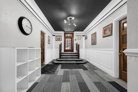 A hallway with a clock on the wall and a staircase in the background at Pleasant Oak Apartments, Oak Park