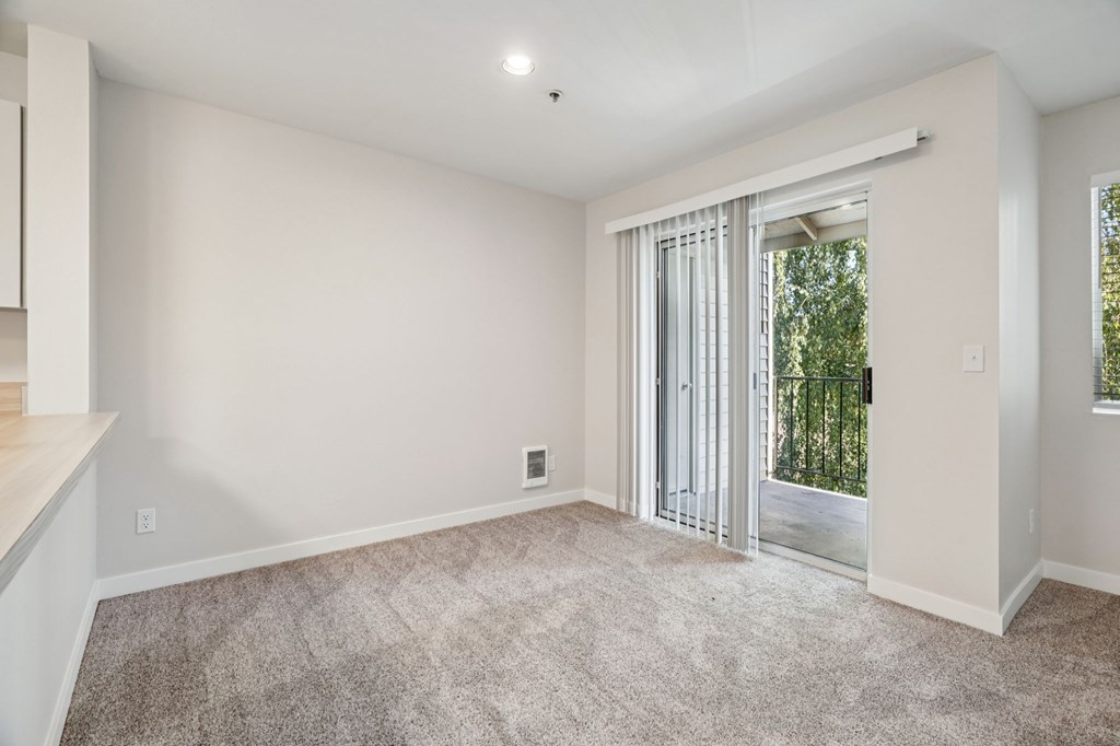 A room with a carpeted floor and a sliding glass door leading to a balcony.