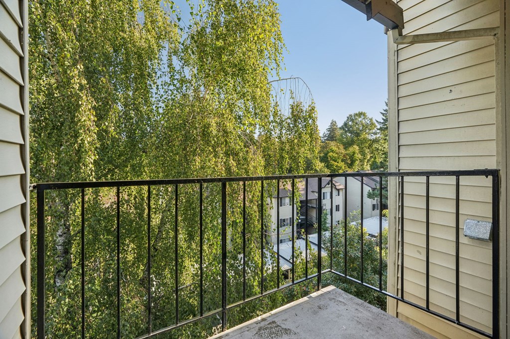 A balcony with a black railing overlooks a tree-filled street.