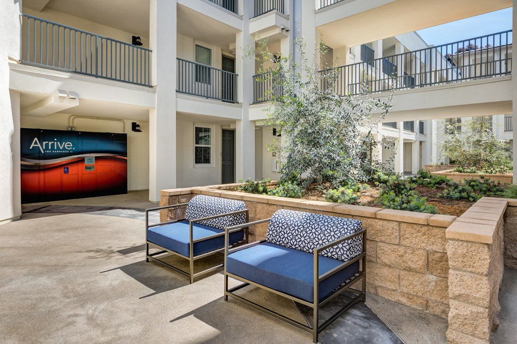 a seating area with two blue chairs and a stone wall in front of a building