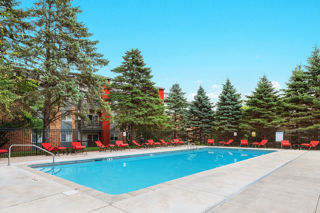 a swimming pool with red chairs around it in front of a building