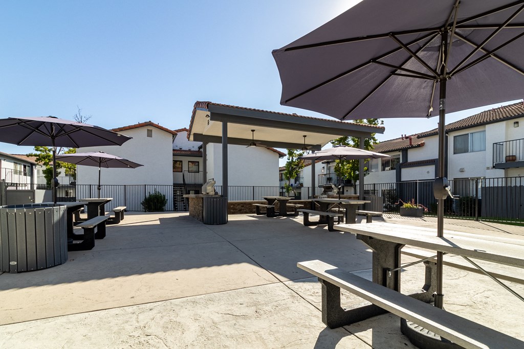 a patio with picnic tables and umbrellas in front of buildings at Alturas Paso Robles Apartment Homes, Paso Robles
