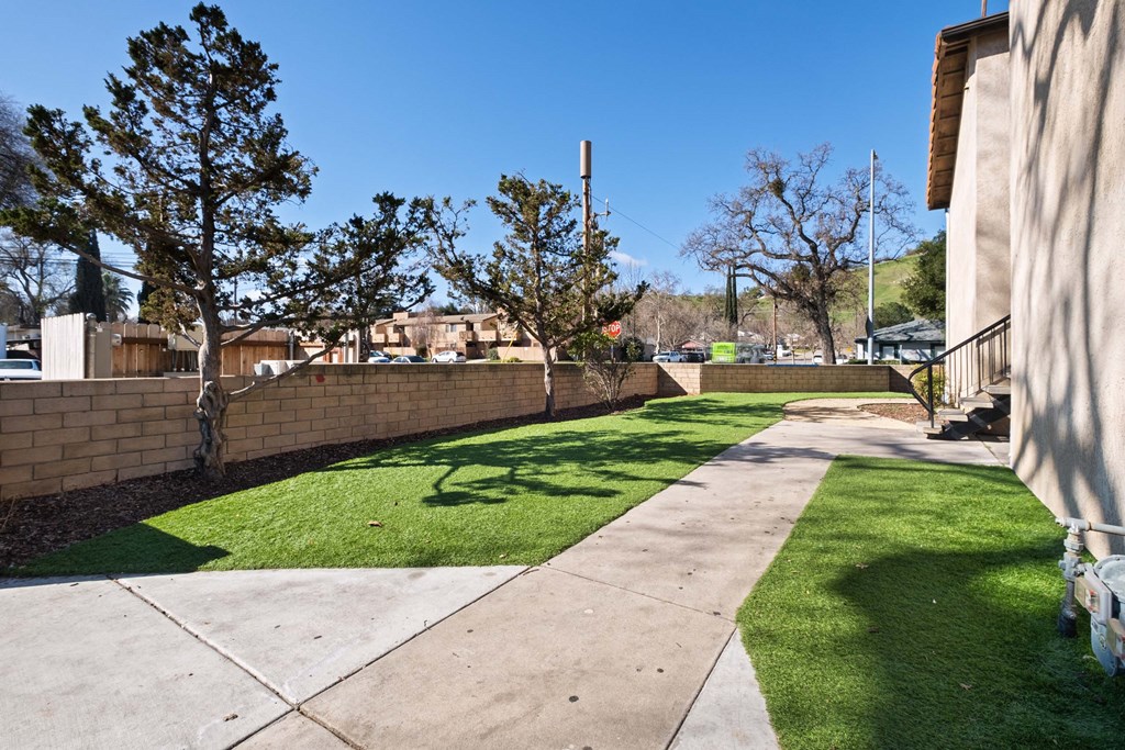 a yard with green grass and a stone wall at Alturas Paso Robles Apartment Homes, Paso Robles