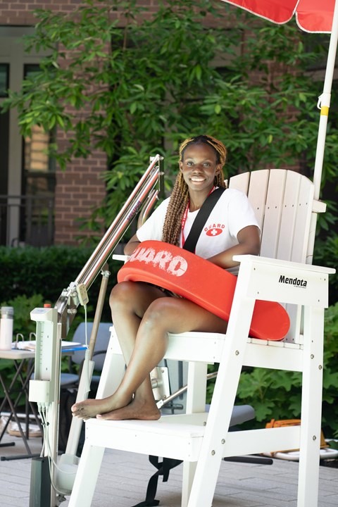 A woman is sitting on a white chair with a red cushion and a red umbrella.
