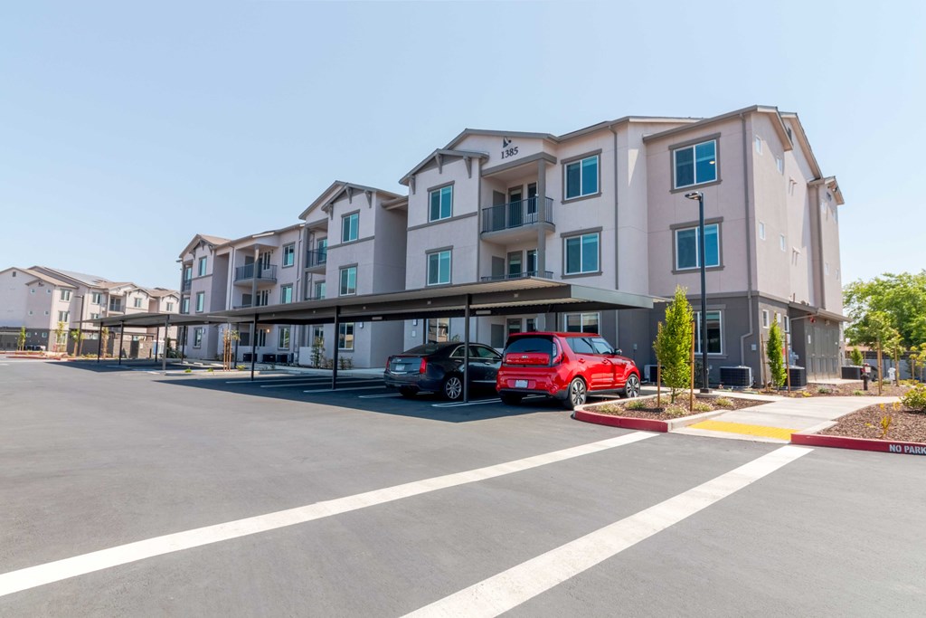 A red car is parked in front of a multi-story apartment building.