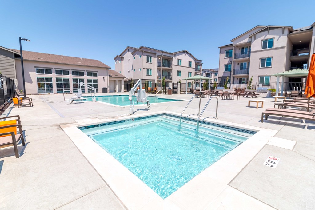 A hot tub with a swimming pool and apartment buildings in the back