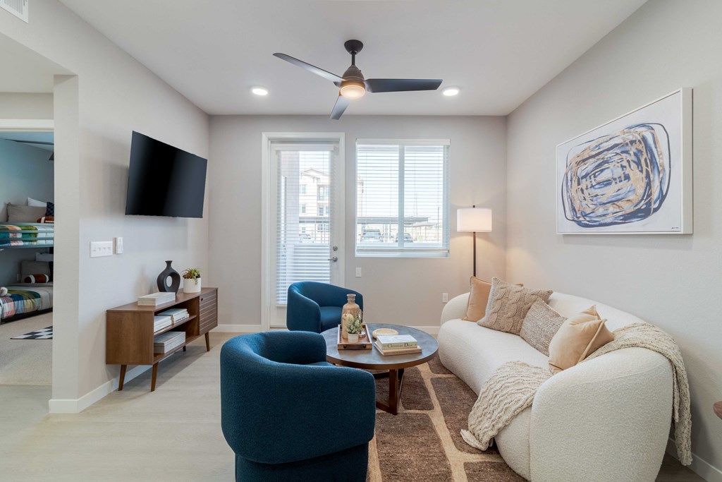A living room with a blue armchair, a white sofa, and a ceiling fan.