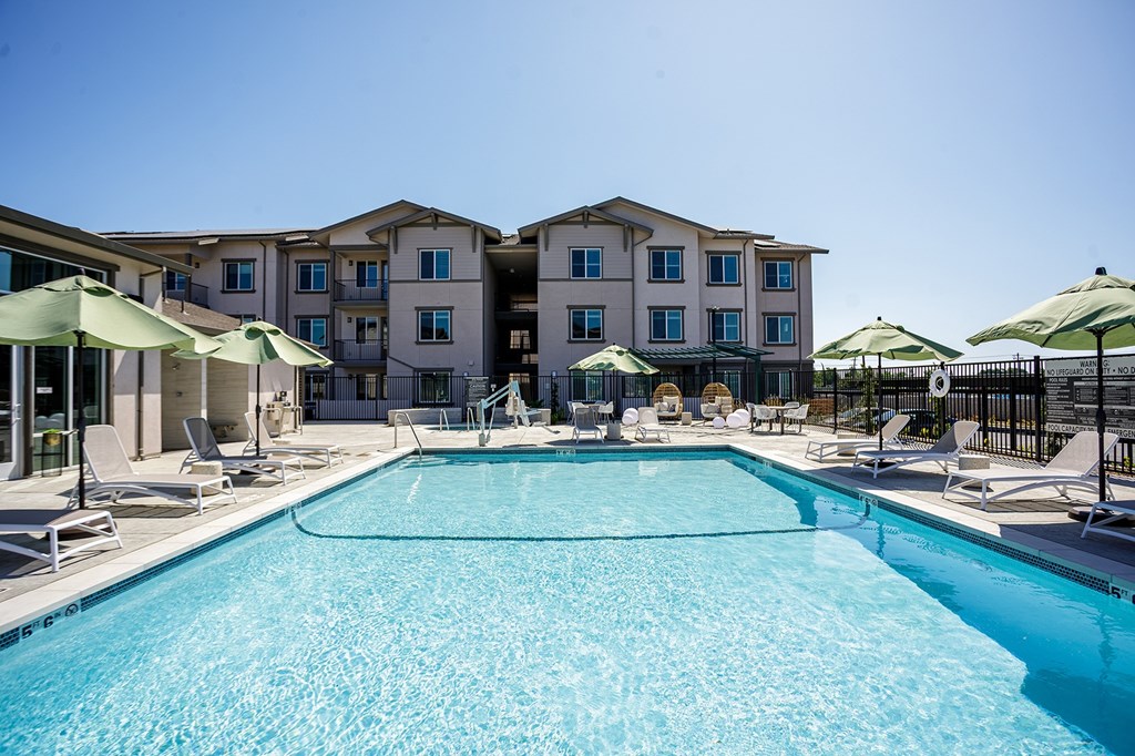 A large swimming pool in front of a building with lounge chairs and umbrellas.