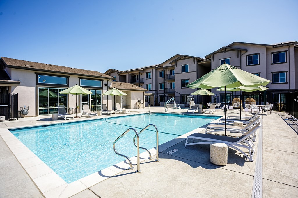 A swimming pool with sun loungers and umbrellas in front of apartment buildings.