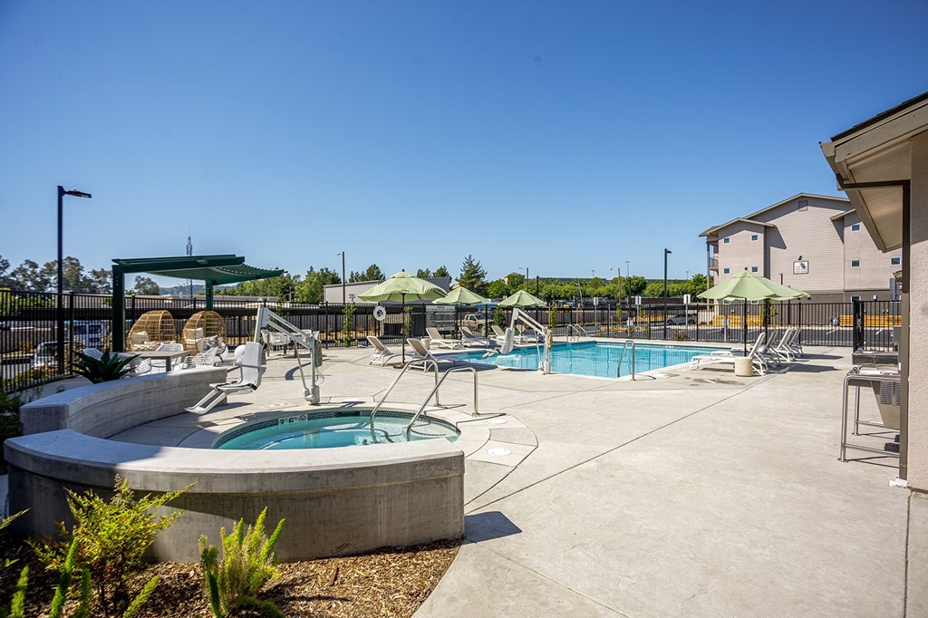A large outdoor swimming pool with a hot tub and lounge chairs.