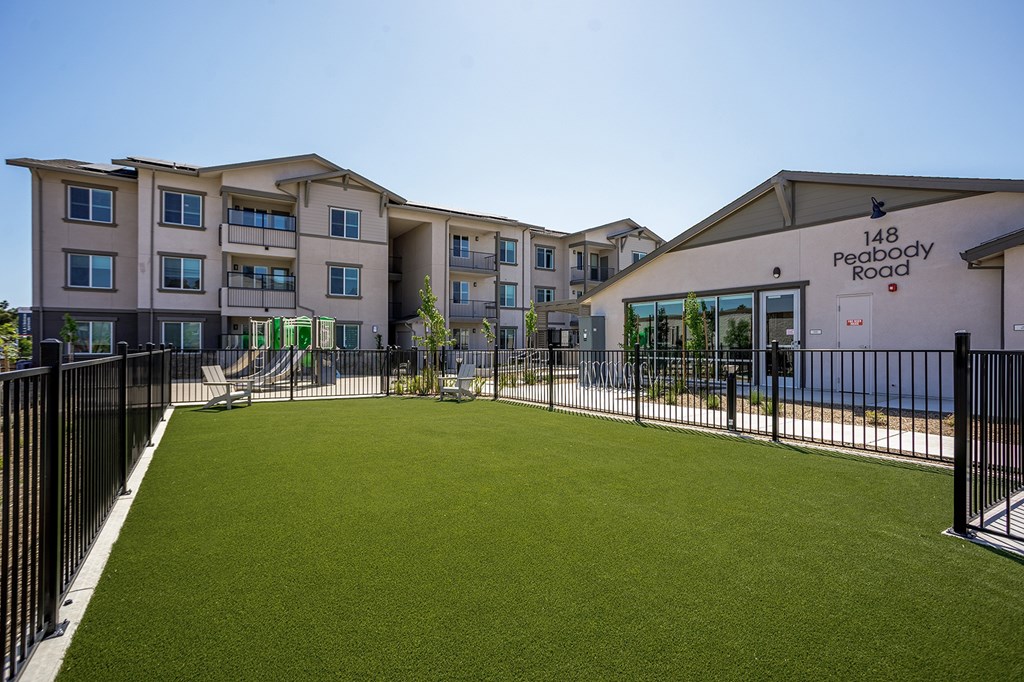 A grassy dog park in front of an apartment building