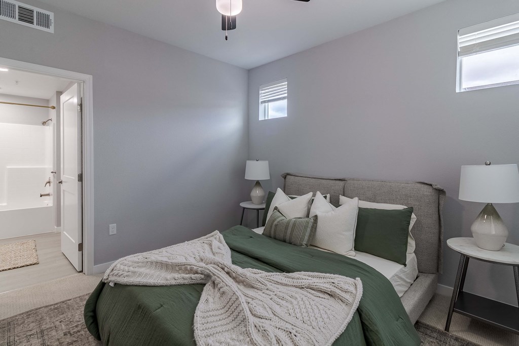 A bedroom with a bed covered in a green blanket and pillows.