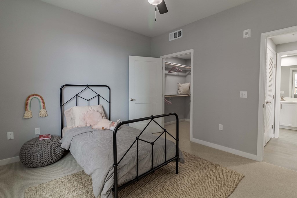 A bedroom with a bed, a rug, a ceiling fan, and a door leading to another room.