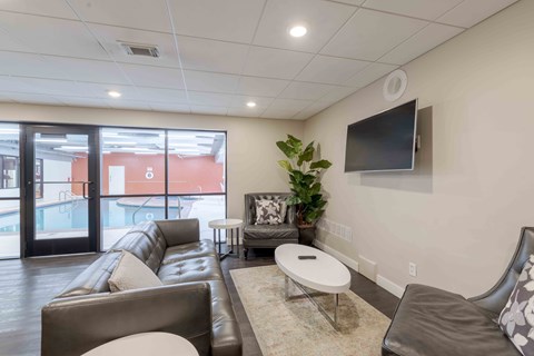 A living room with a brown leather couch, a white coffee table, and a flat screen TV mounted on the wall.